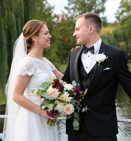 Bride in wedding dress and veil stands face to face with the groom in a black tuxedo